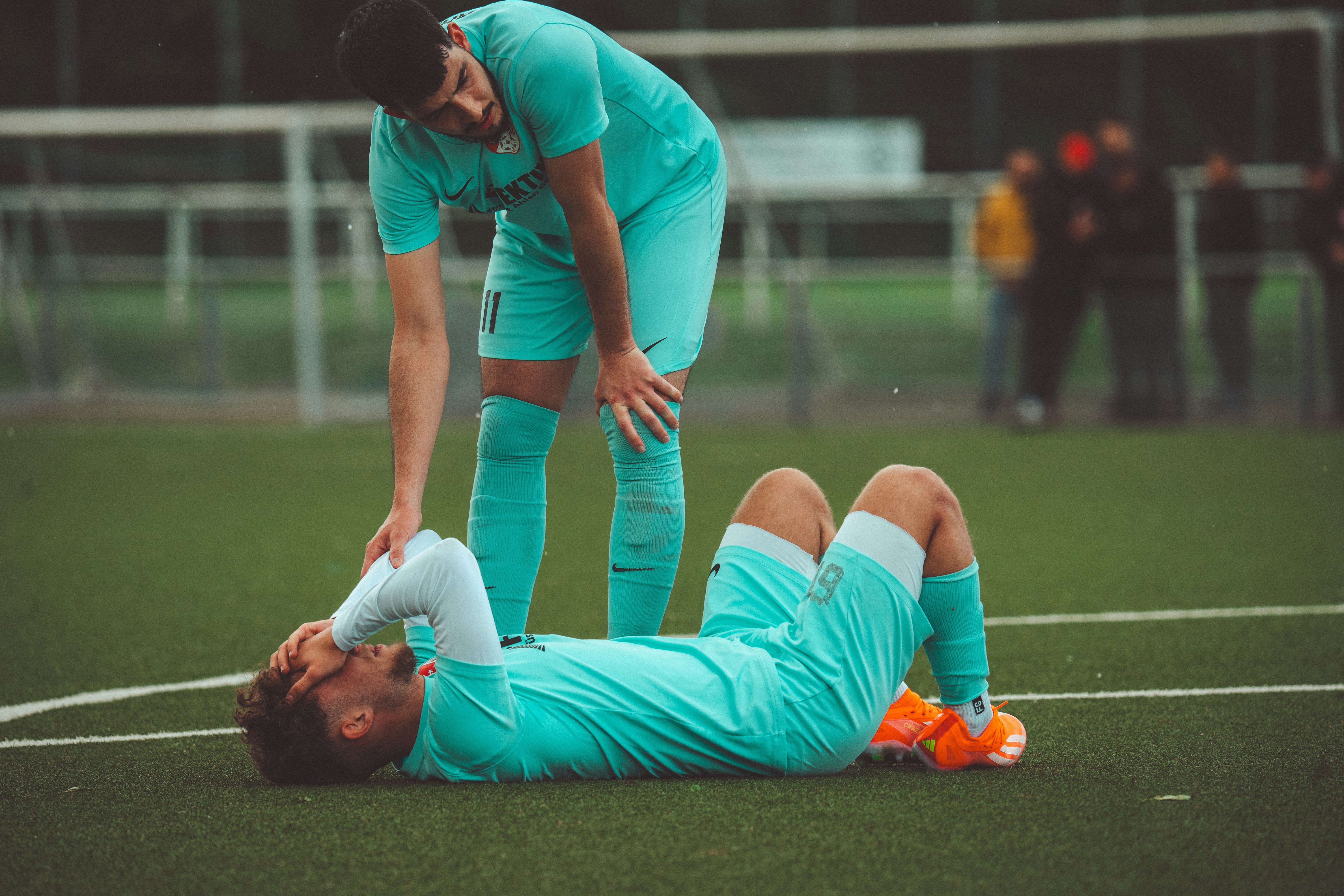 Football player lying on the pitch as a teammate checks on him.